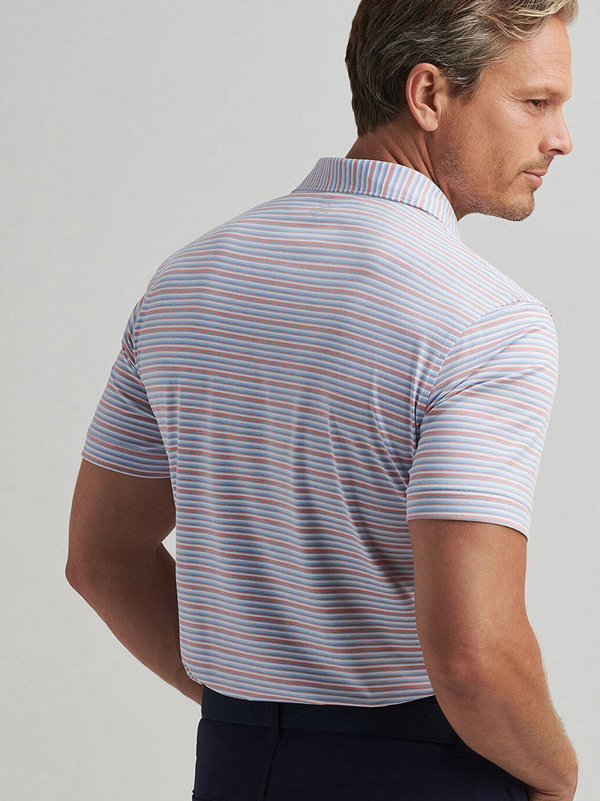 A man faces away, wearing the Peter Millar Cadence Performance Jersey Polo in Blue Frost with short sleeves, a collar, blue, pink, and white stripes, and UPF 50+ sun protection.