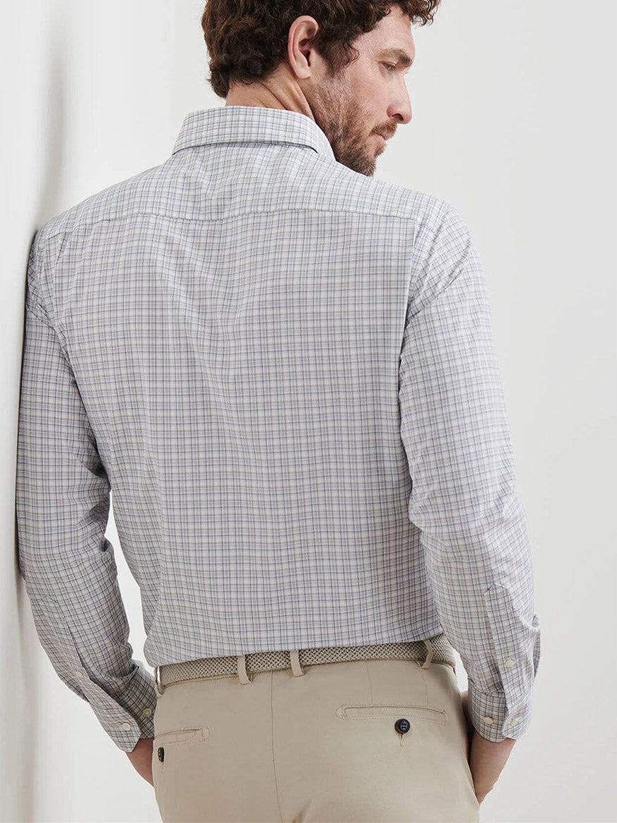 A man is seen from behind wearing a Peter Millar Carter Performance Poplin Sport Shirt in Nebula Blue, long-sleeved and tucked into beige pants with a woven belt.