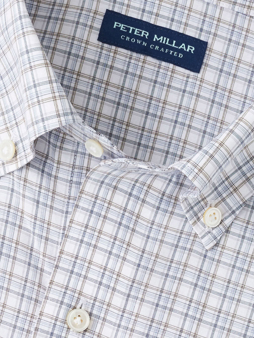 Close-up of a Peter Millar Carter Performance Poplin Sport Shirt in Nebula Blue, featuring a men’s four-way stretch fabric with a blue, brown, and white plaid pattern and a "Peter Millar Crown Crafted" label.