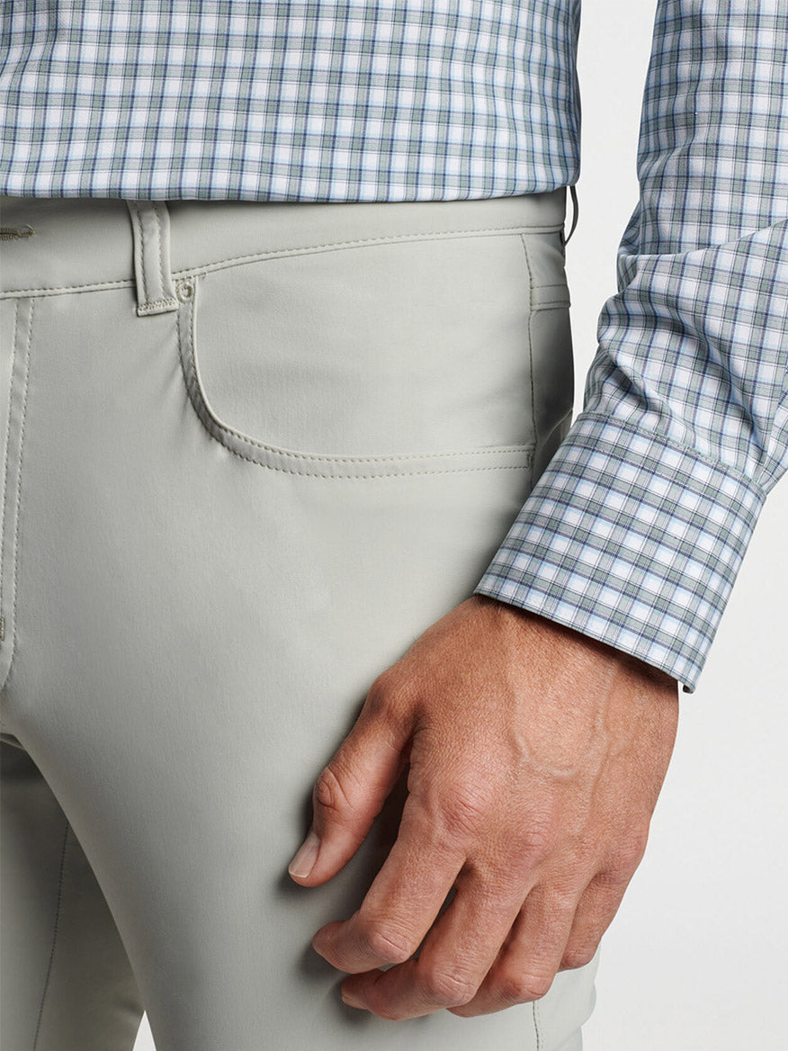 Close-up of a man's hand in his pocket, wearing light gray pants and a Peter Millar Cole Performance Poplin Sport Shirt Sage Fog with UPF 50+ sun protection.