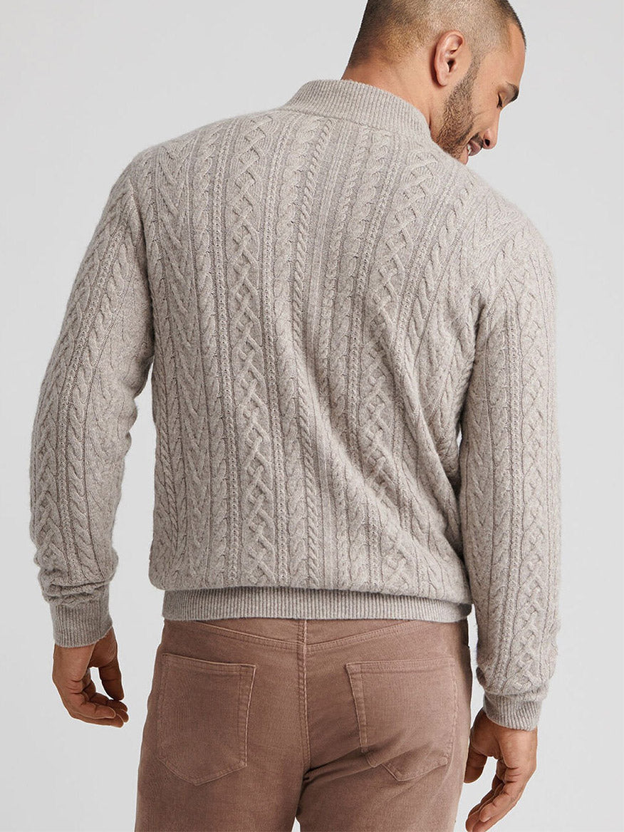 A man faces away in a Peter Millar Crescent Ridge Cable Quarter-Zip Sweater in Light Elm and light brown pants, standing against a plain background.