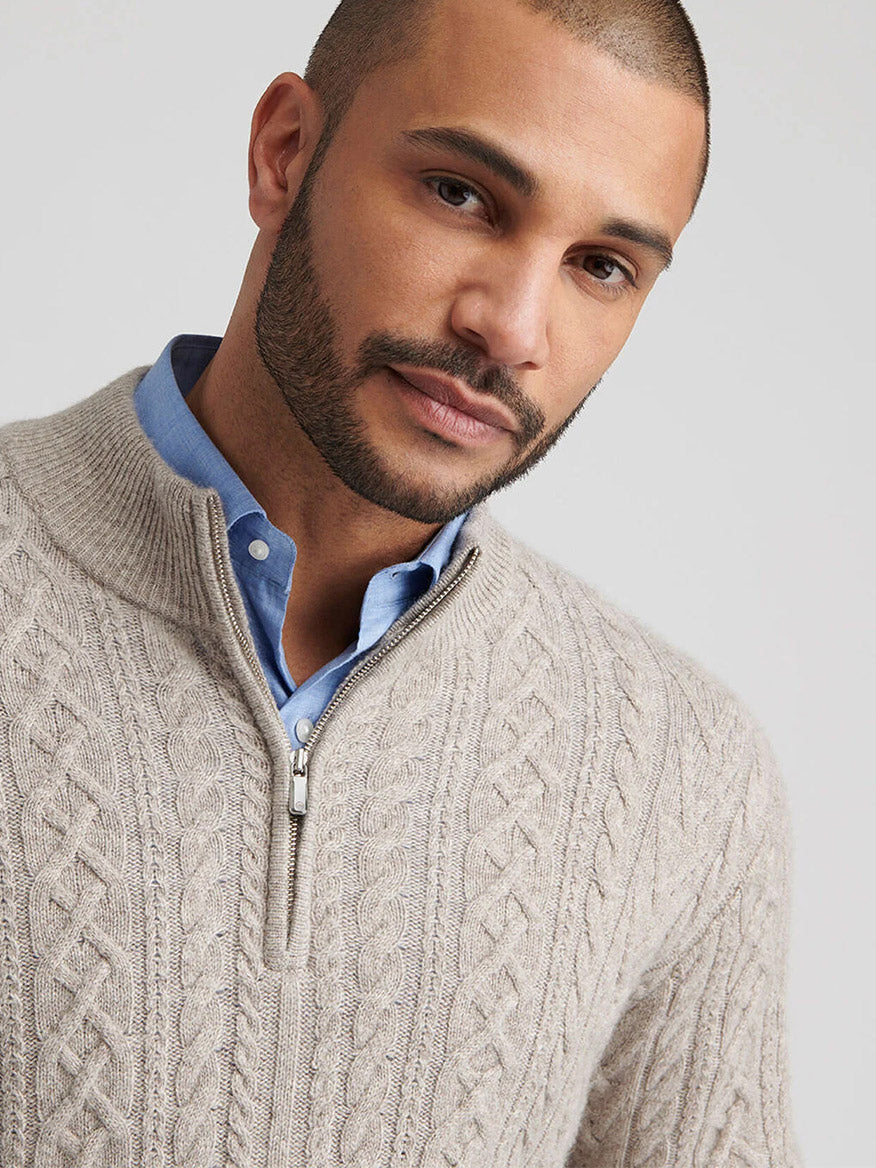 A man with short hair and a beard wears the Peter Millar Crescent Ridge Cable Quarter-Zip Sweater in Light Elm over a blue collared shirt, looking at the camera.