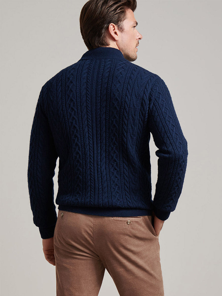 A man faces away from the camera wearing the Peter Millar Crescent Ridge Cable Quarter-Zip Sweater in Navy and light brown pants, set against a plain background.