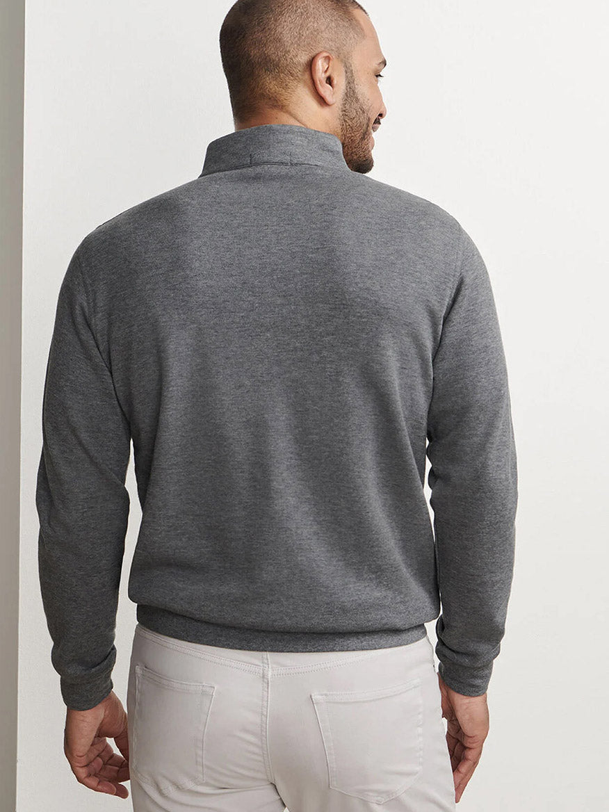 A man stands facing away, wearing the Peter Millar Crown Comfort Pullover in Charcoal—featuring four-way stretch—and light-colored pants, set against a plain white background.