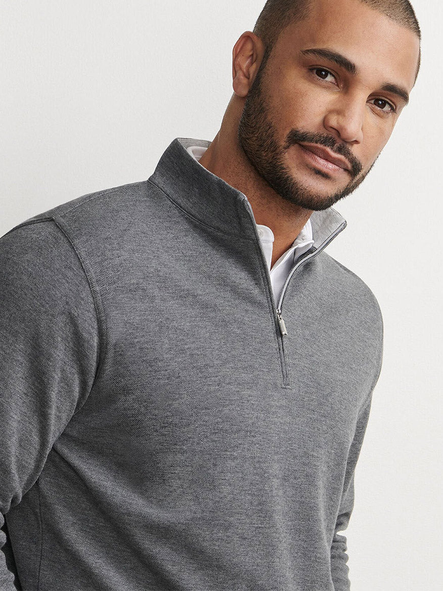 A man with short hair and a beard wears the Peter Millar Crown Comfort Pullover in Charcoal over a white collared shirt, standing against a plain light background.