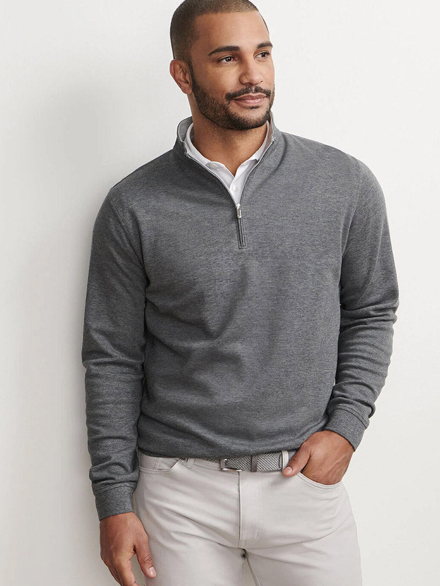A man models the Peter Millar Crown Comfort Pullover in Charcoal over a white collared shirt and light pants against a plain background, highlighting this lightweight, versatile layer.