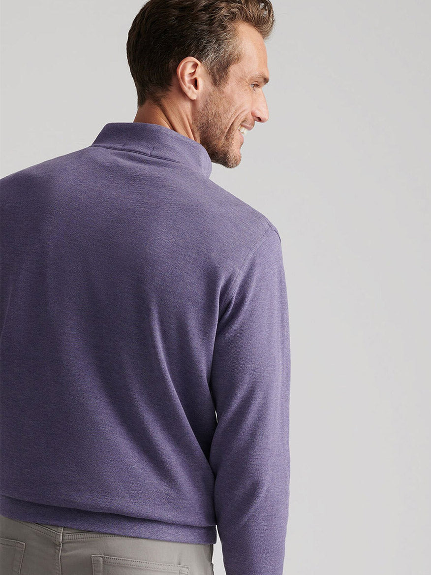 A man with short brown hair, seen from behind, wears the Peter Millar Crown Comfort Pullover in Deep Violet and gray pants, standing against a plain background.