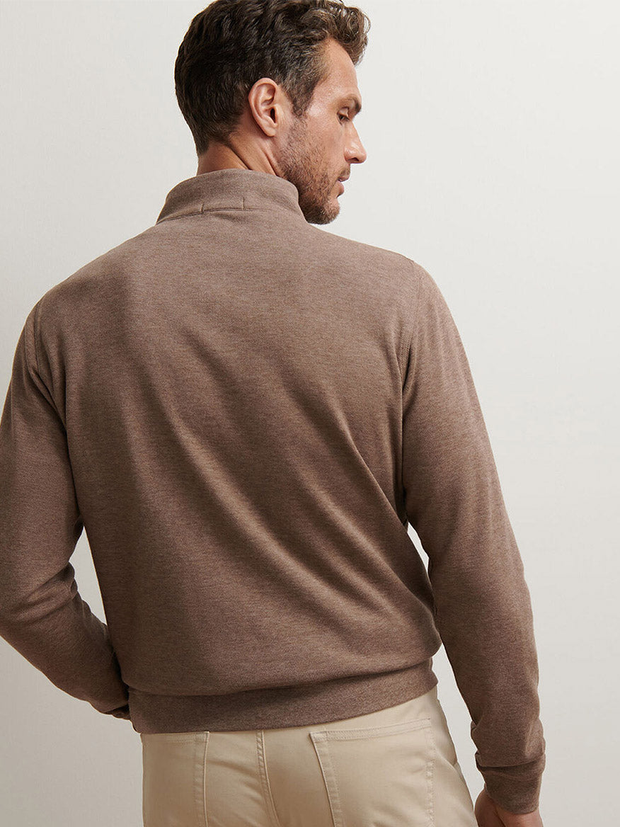 A man faces away from the camera, wearing the Peter Millar Crown Comfort Pullover in Poplar Brown—an ideal lightweight layer—with beige pants, set against a plain light-colored background.