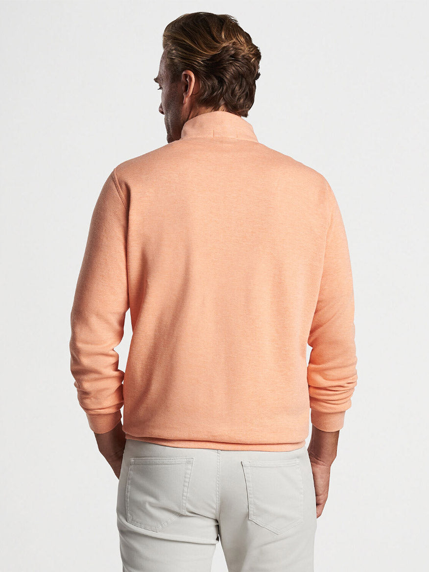 Man viewed from behind wearing a Peter Millar Crown Comfort Pullover in Coral Haze and light gray pants.