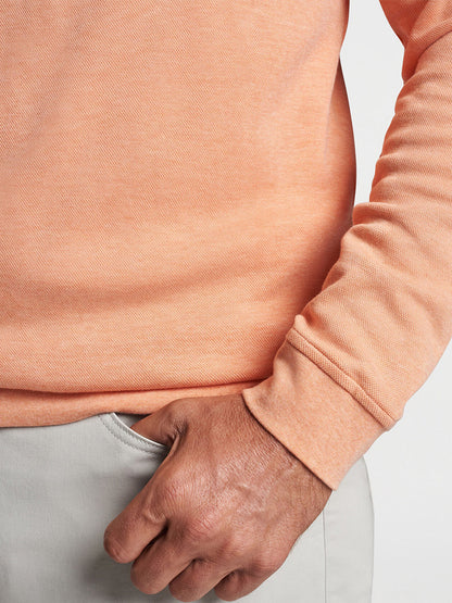 Close-up of a person wearing a Peter Millar Crown Comfort Pullover in Coral Haze and light gray pants, with hand partially inserted into a pocket.