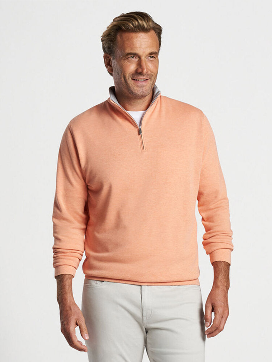 Man in a Peter Millar Crown Comfort Pullover in Coral Haze and beige pants posing with a slight smile.