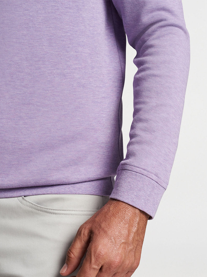 Close-up of a person wearing a Peter Millar Crown Comfort Pullover in Wild Lilac and light grey pants, with their hand resting on their hip.
