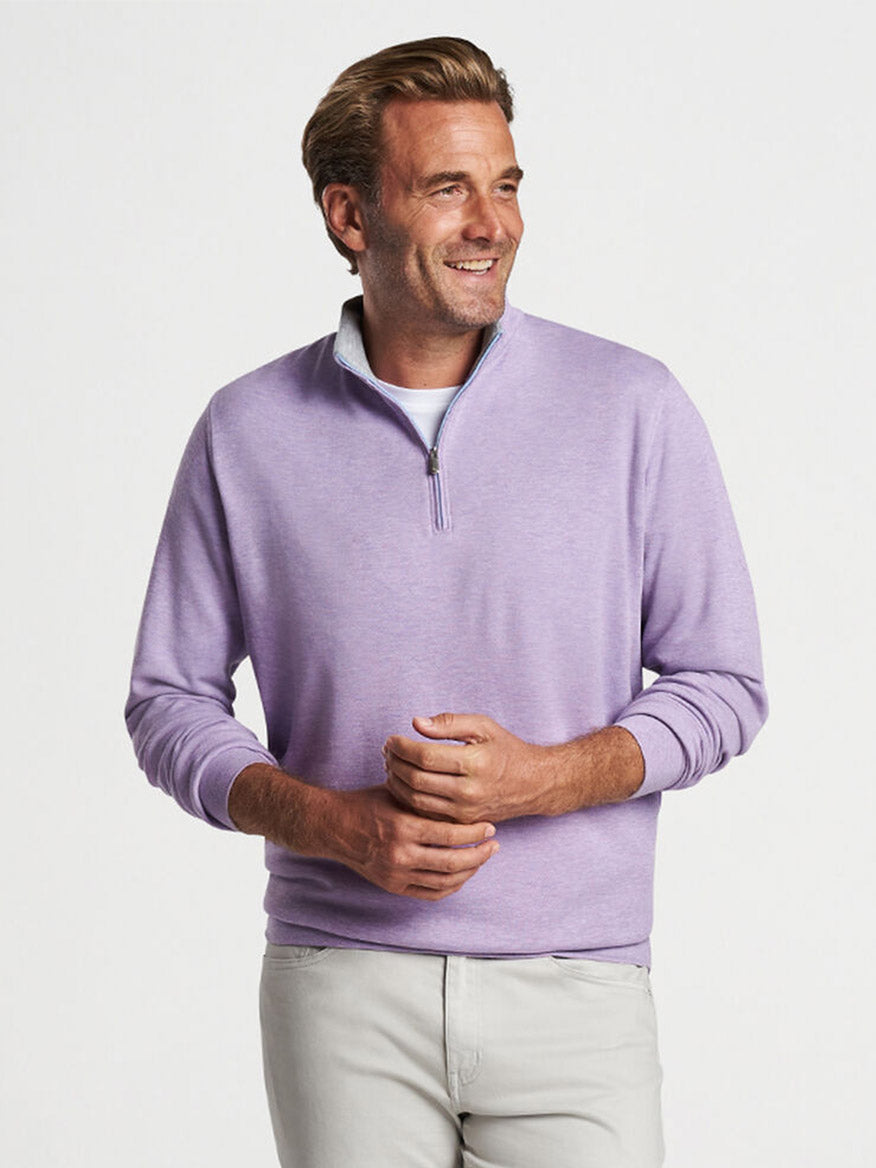 A man smiling while wearing a Peter Millar Crown Comfort Pullover in Wild Lilac and light-colored pants.