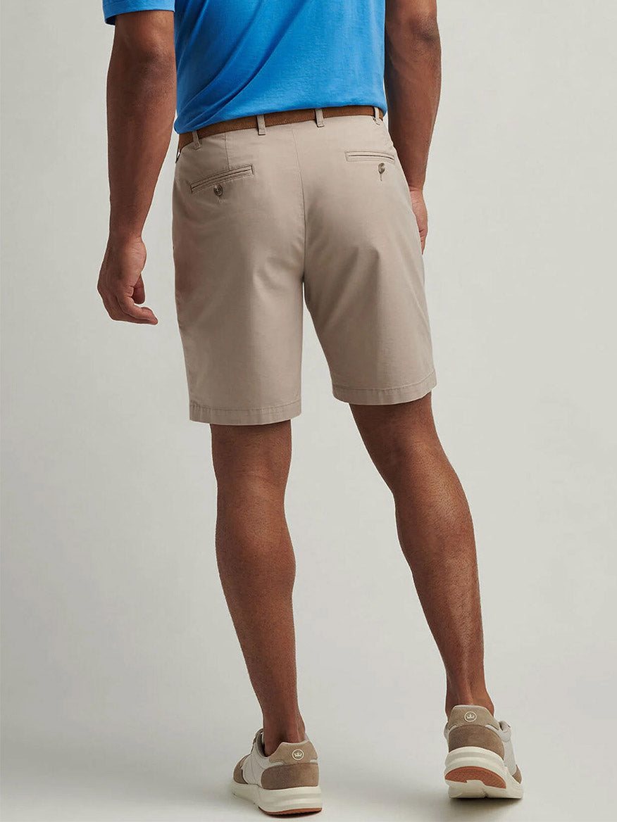 A man faces away, wearing a blue polo shirt, beige sneakers, and Peter Millar Crown Comfort Short in Khaki against a plain background.