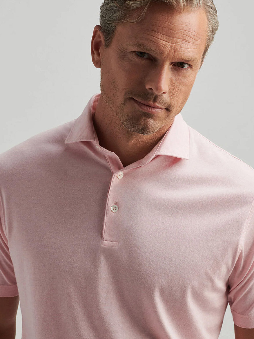 A man with light hair wears a Peter Millar Excursionist Flex Polo in Pink Crepe, featuring a heathered design, and stands against a plain light gray background.