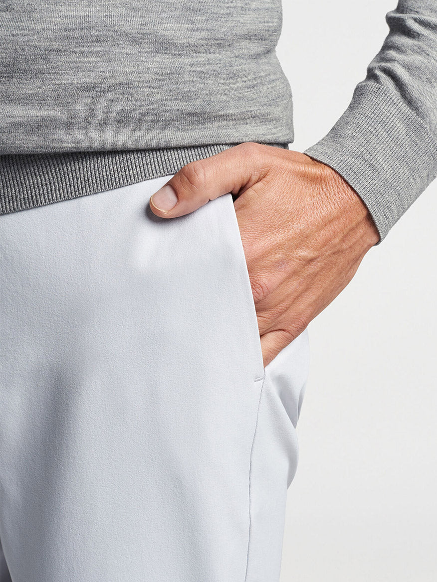 Person tucking a Peter Millar Excursionist Flex Quarter-Zip in Gale Grey into light-colored pants.