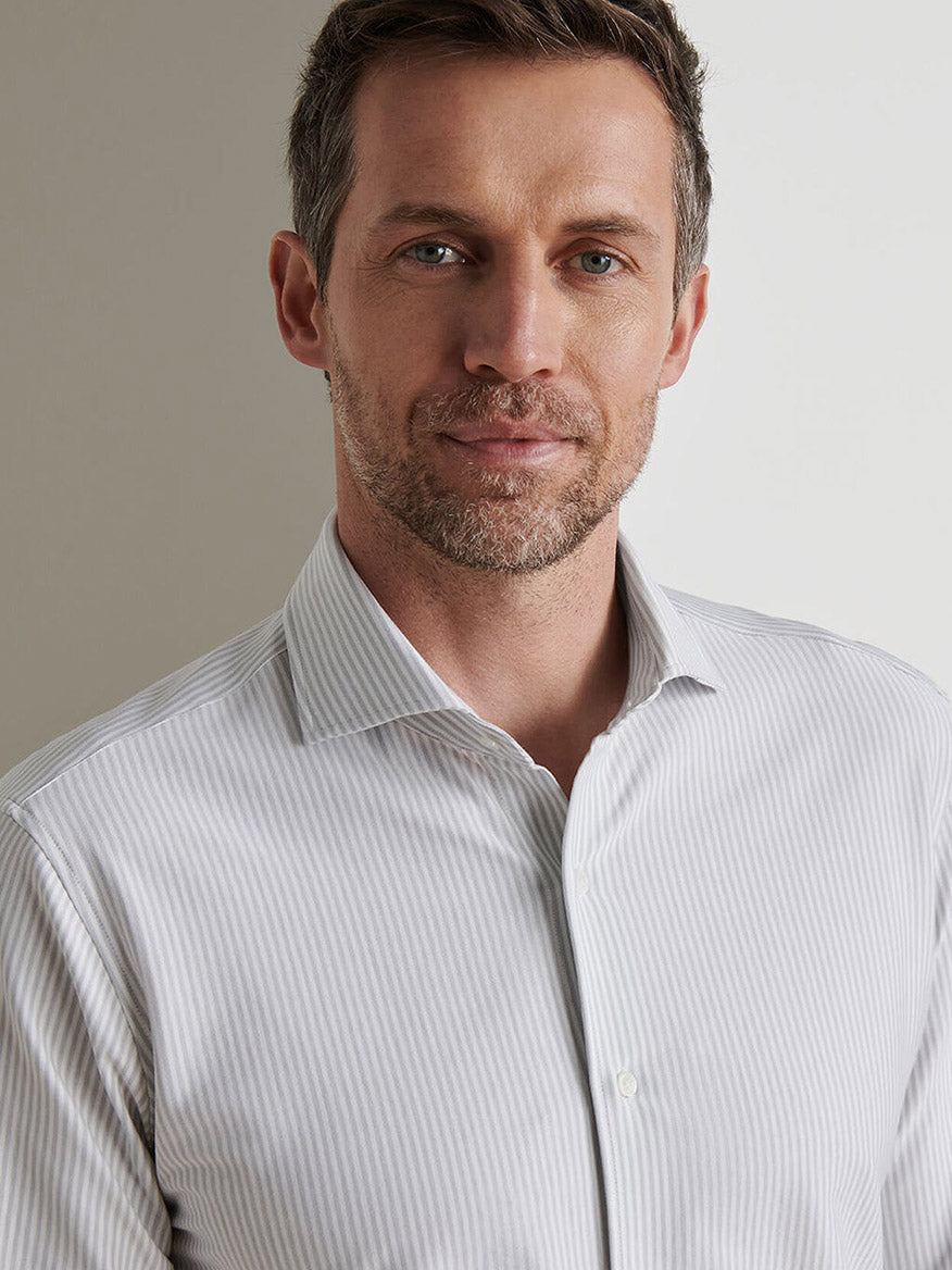 A man with short brown hair and light stubble wears a Peter Millar Excursionist Flex Stripe Sport Shirt in British Grey, made from cotton-stretch fabric, standing against a plain background.
