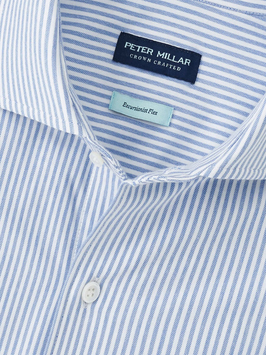 Close-up of the Peter Millar Excursionist Flex Stripe Sport Shirt in Rain Cloud, showing blue and white stripes with "Crown Crafted" and "Excursionist Flex" labels—a stylish cotton-stretch shirt designed for refined comfort.
