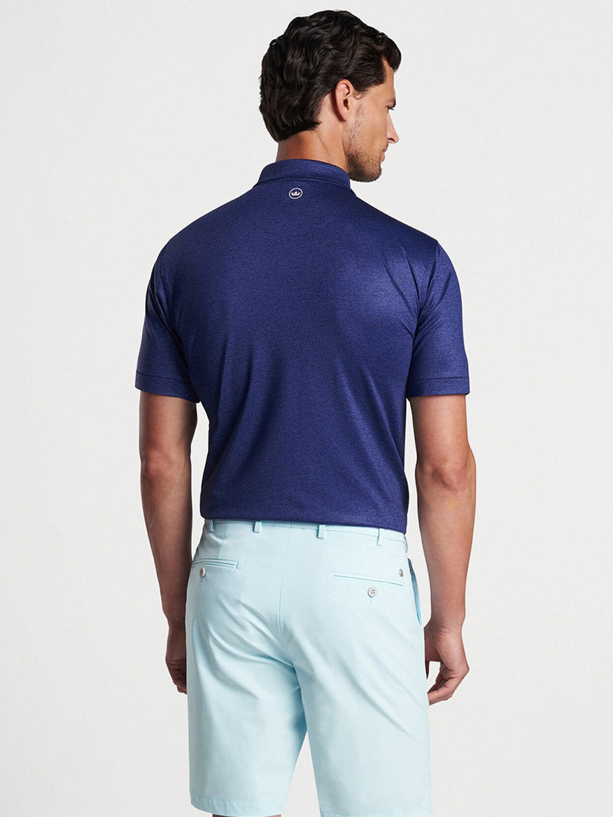 Man wearing a Peter Millar Instrumental Nouveau Performance Jersey Polo in Navy and light blue trousers viewed from the back.