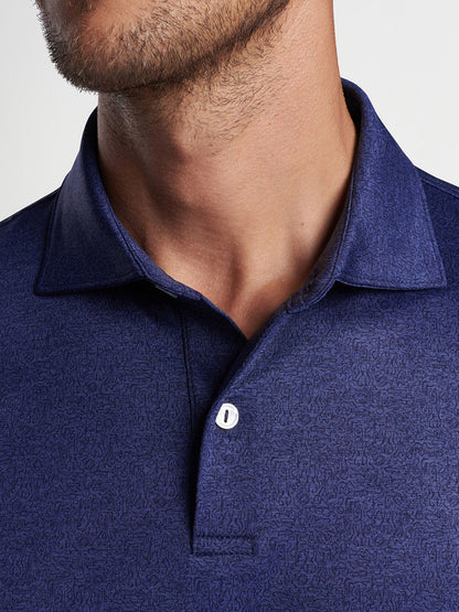 Close-up of a man wearing a tailored fit navy blue Peter Millar Instrumental Nouveau Performance Jersey Polo with a patterned design.