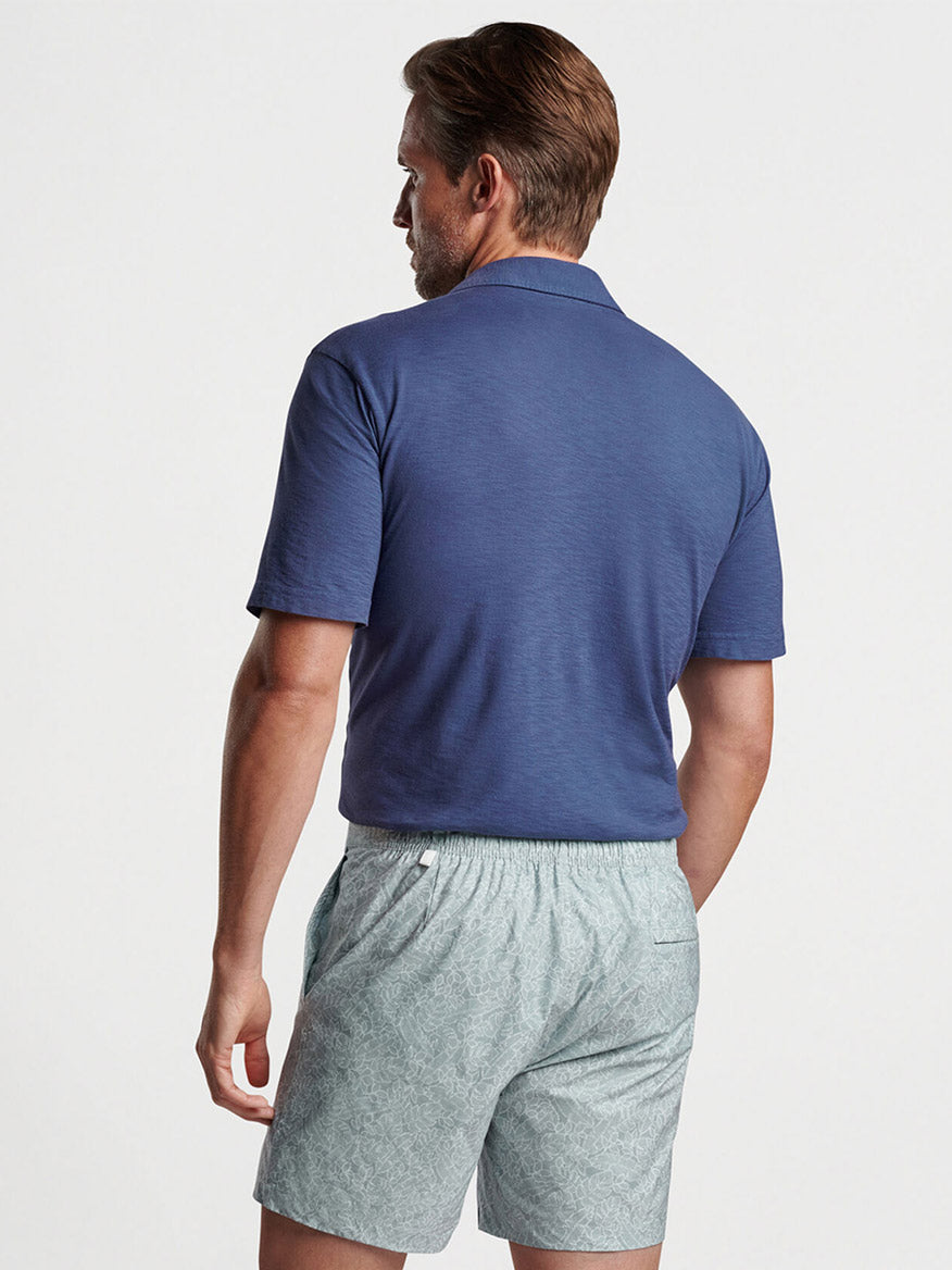 A man viewed from behind wearing a tailored fit Peter Millar Journeyman Short Sleeve Polo in Navy and grey shorts.