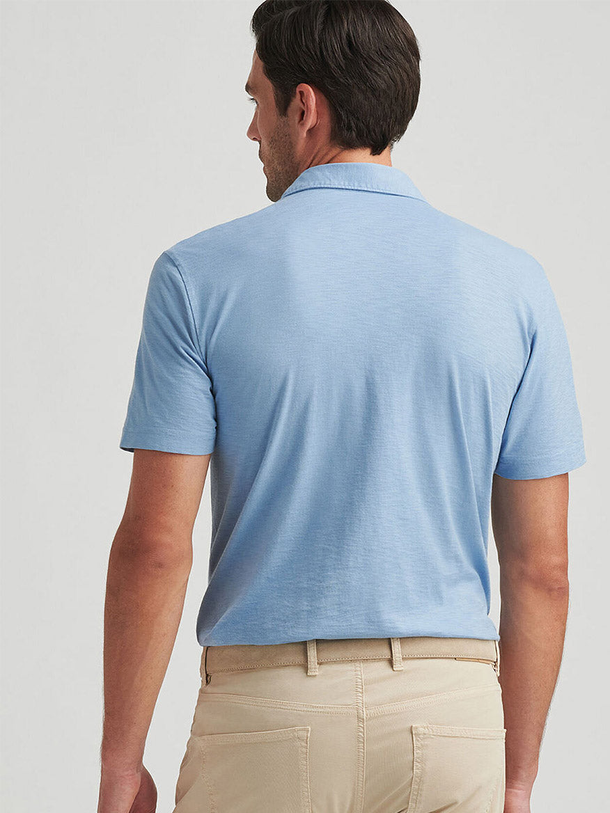 A man stands with his back to the camera, wearing the Peter Millar Journeyman Short Sleeve Polo in Angelite and beige pants, highlighting the polo’s modern tailored fit.