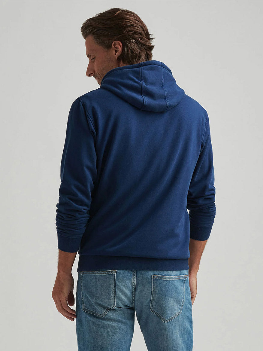 A person stands facing away from the camera, wearing the Peter Millar Lava Wash Hoodie in Navy and light blue jeans against a plain background.