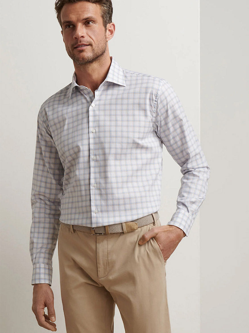 A man wearing the Peter Millar Lenox Crown Lite Cotton-Stretch Sport Shirt in White and beige pants stands against a plain light-colored wall, looking slightly to the side.