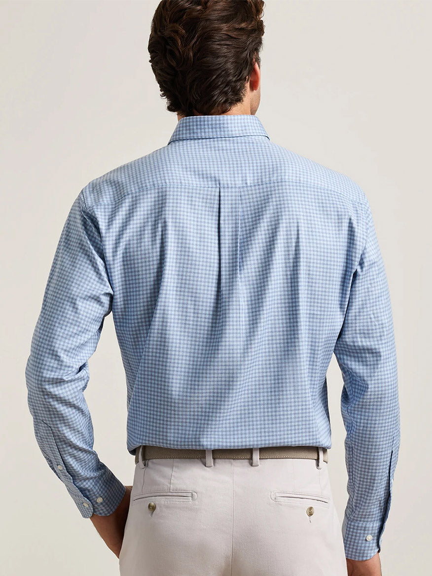 A man is seen from behind, wearing the Peter Millar Liam Crown Soft Twill Sport Shirt in Blue Freesia—crafted from a stretch performance fabric with a light blue checkered pattern—paired with light-colored pants and a belt, set against a plain background. This easy-care shirt offers everyday comfort and style.