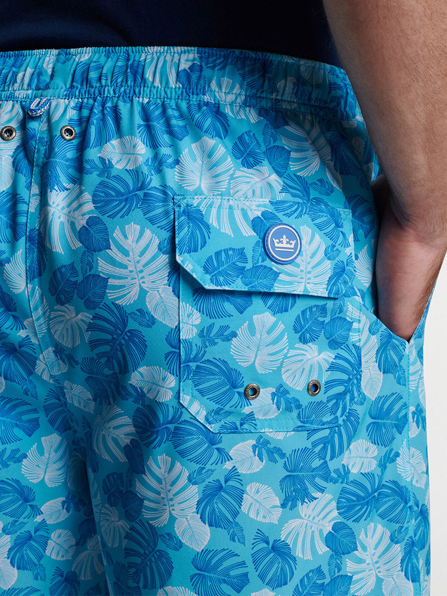 Close-up of a person wearing blue Peter Millar Linework Monstera Swim Trunk in Seasalt with a hand in the pocket.