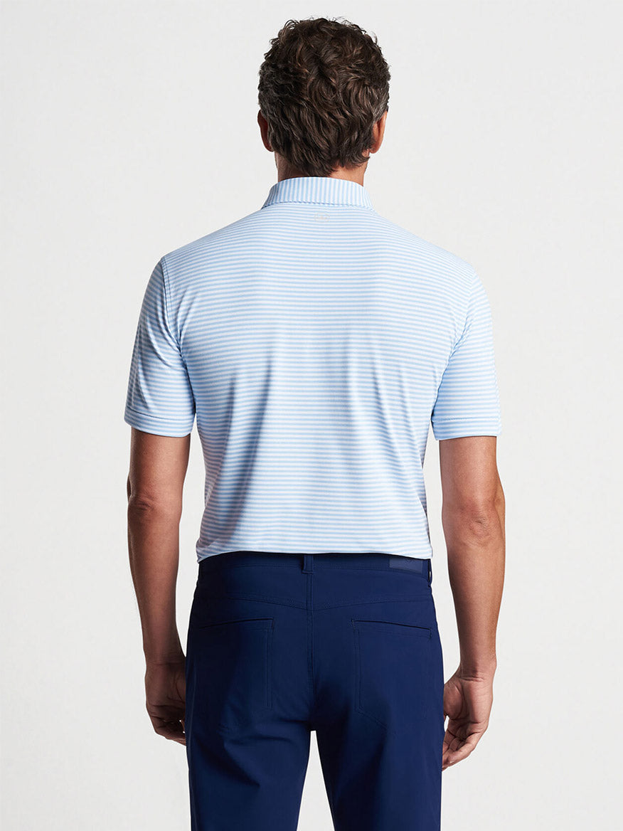 Man standing with his back to the camera wearing a striped Peter Millar Mood Performance Mesh Polo in Blue Frost and navy blue trousers.