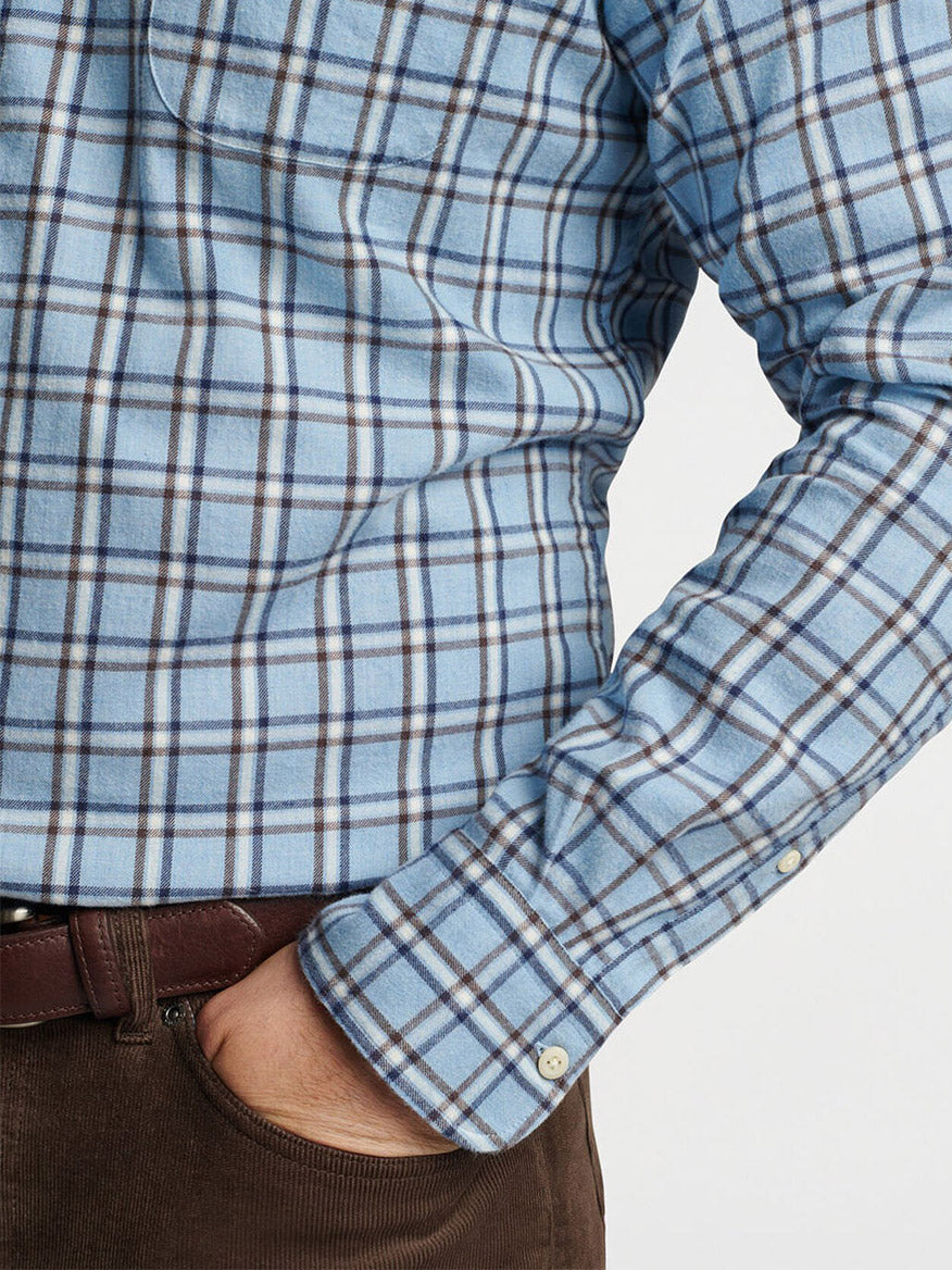 A person is wearing a Peter Millar Nelson Flannelite Cotton-Stretch Sport Shirt in Cottage Blue, with the cuffs buttoned and tucked into brown pants secured by a belt. The shirt's fabric provides just enough stretch for easy movement. Only the torso and a hand resting in the pocket are visible.