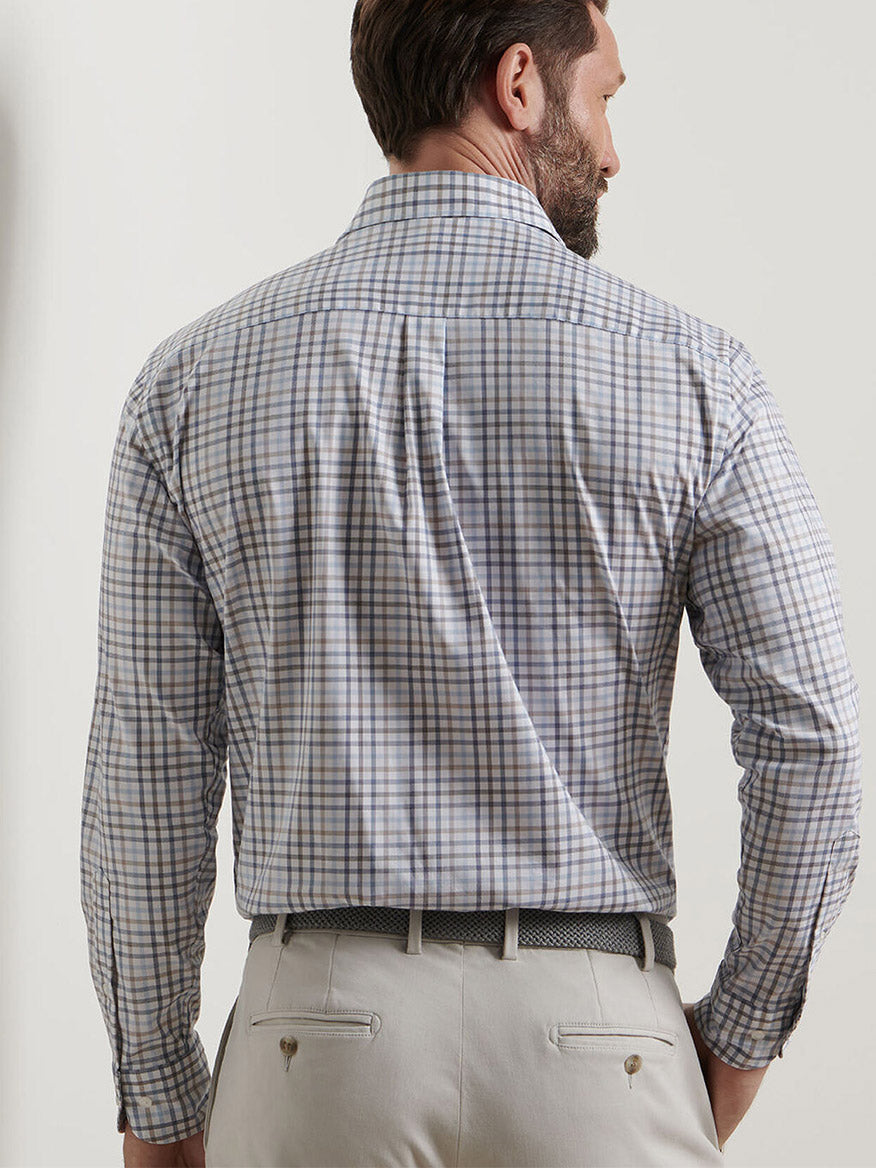 Seen from behind, a man wears the Peter Millar North Coast Crown Lite Cotton-Stretch Sport Shirt in Blue Haze—its classic fit and easy-care fabric offer timeless style, tucked neatly into beige pants with a patterned belt.