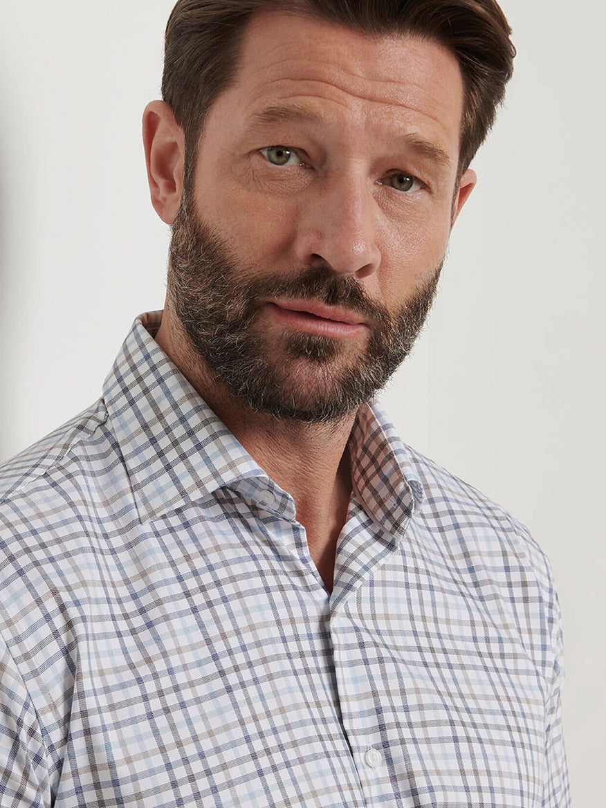 A man with brown hair and a beard wears the Peter Millar North Coast Crown Lite Cotton-Stretch Sport Shirt in Blue Haze, standing against a plain light background.