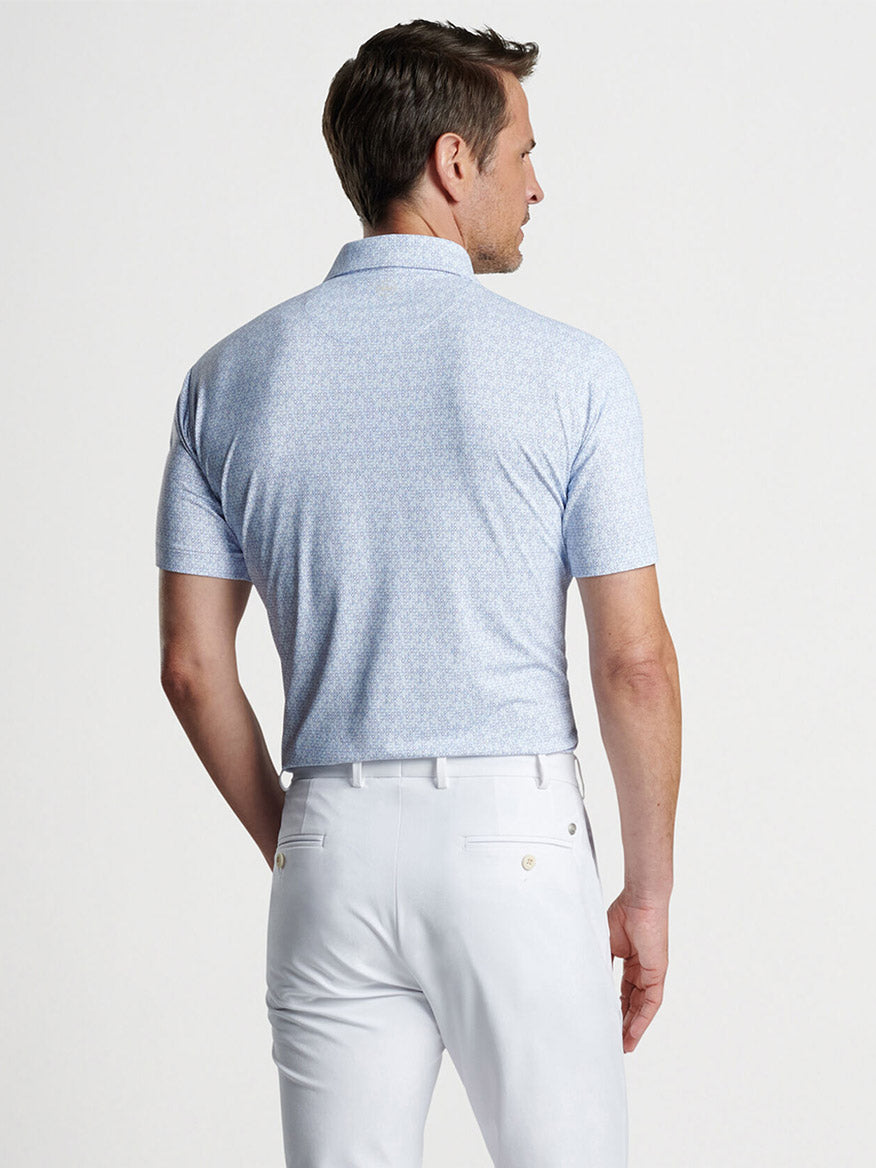 Man wearing a Peter Millar Rhythm Performance Jersey Polo in White/Blue Pearl with UPF 50+ sun protection and white pants, viewed from the back.
