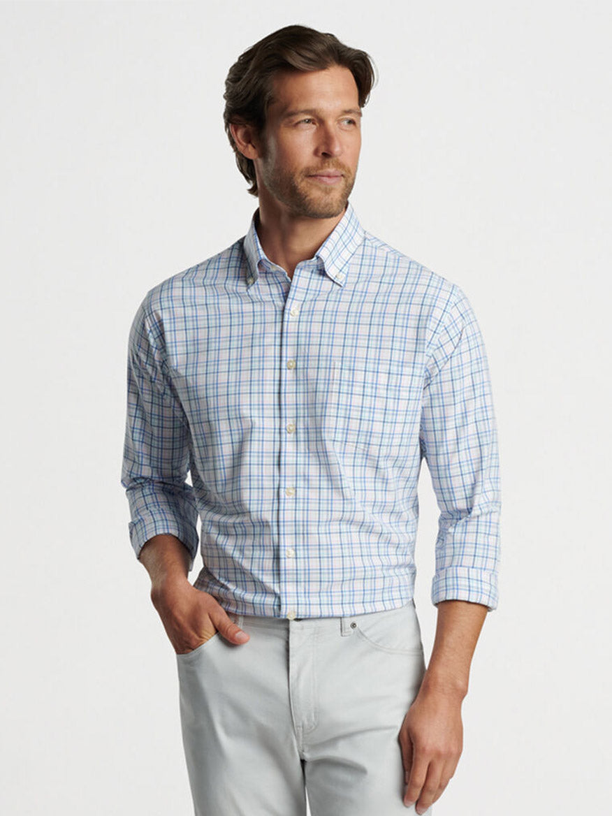 A man wearing a Peter Millar Roxbury Performance Poplin Sport Shirt in Maritime and light-colored pants, gazing to the side.