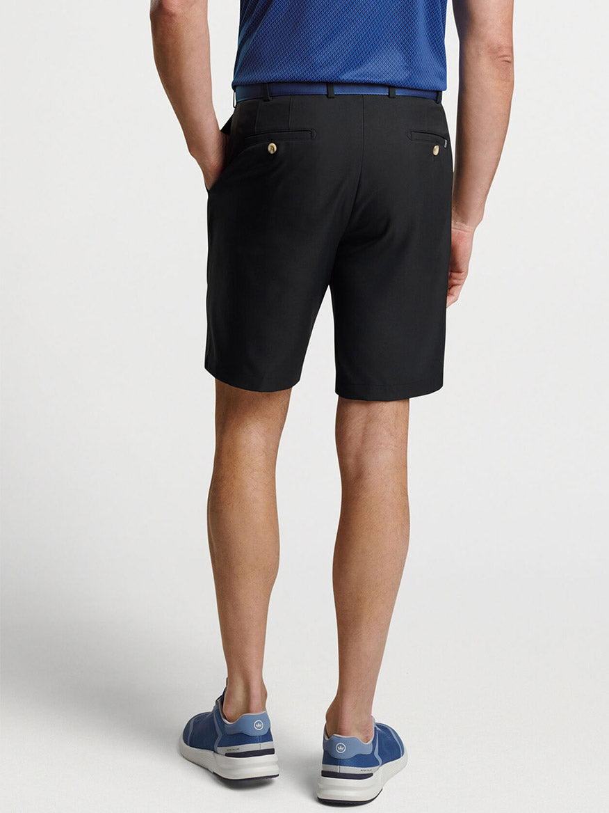 Man standing in Peter Millar Salem Performance Short in Black, blue polo shirt, and blue and white sneakers.