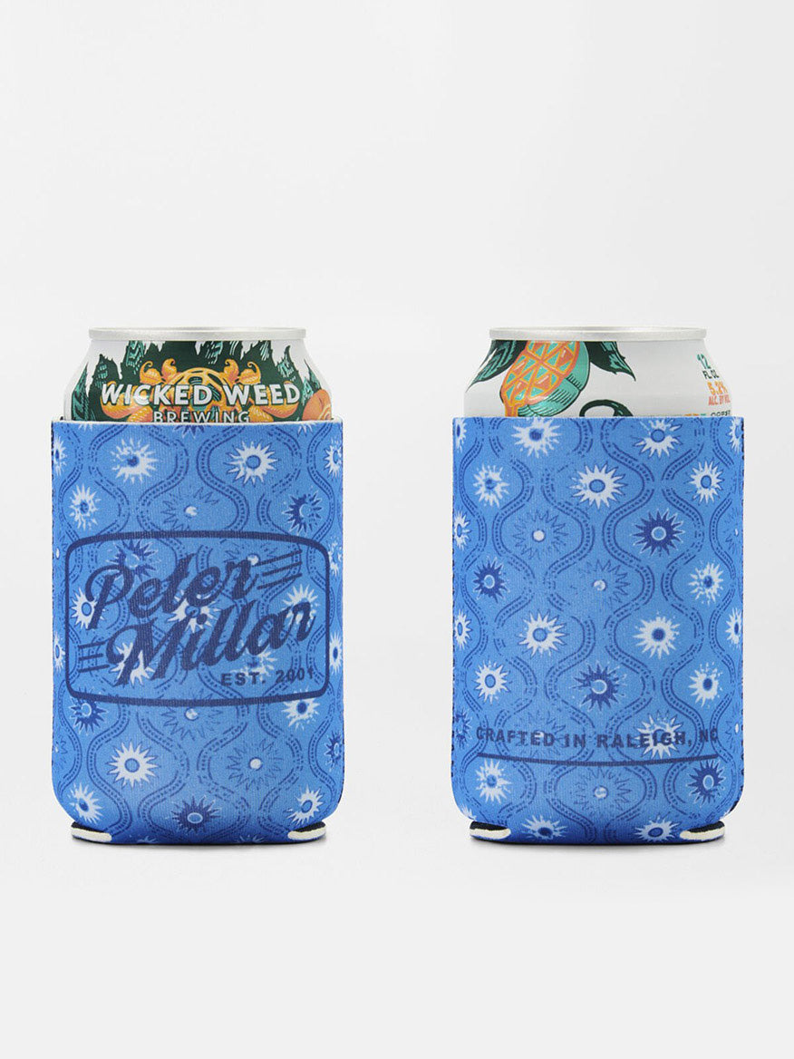 Two cans of Wicked Weed beer are nestled inside blue koozies with exclusive hand-designed floral patterns. One koozie reads "Peter Millar," while the other states "Crafted in Raleigh." Paired with Peter Millar Saltwater Spirits Swim Trunk in Blue Macaw, it's perfect for a beach day.