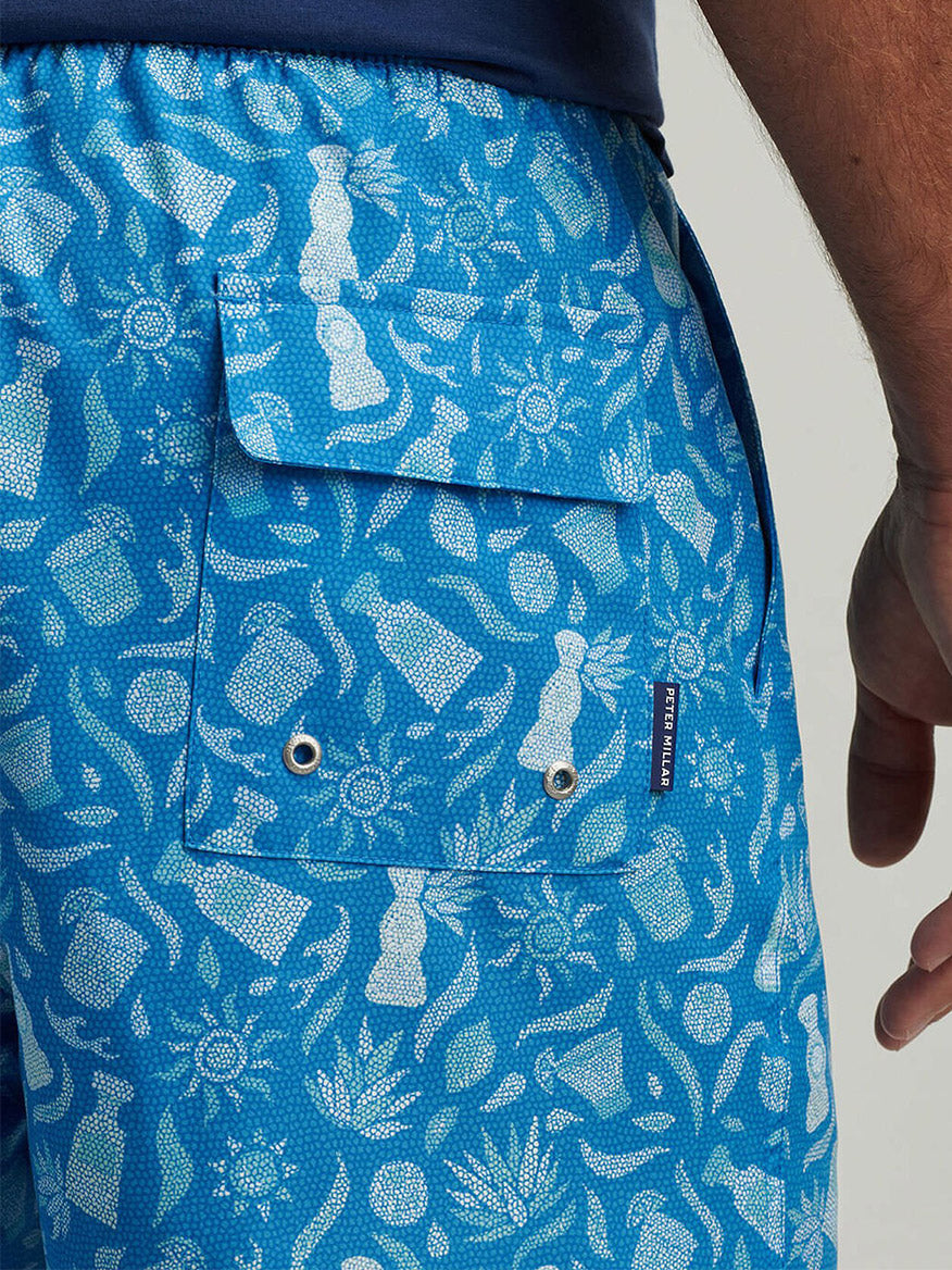 Man wearing the Peter Millar Saltwater Spirits Swim Trunk in Blue Macaw, featuring exclusive hand-designed print and pocket detail.