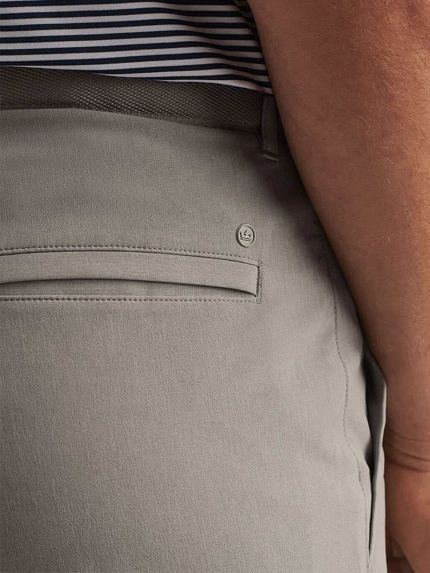 Close-up of a person wearing the Peter Millar Shackleford Performance Hybrid Short in British Grey, featuring a back pocket, brown belt, striped shirt, and crafted from four-way stretch fabric for comfort and flexibility.