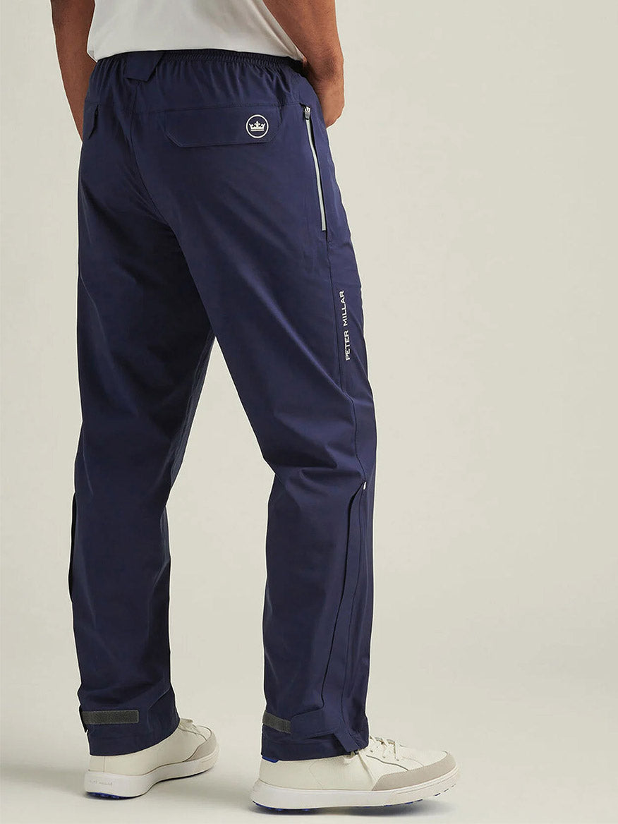 A person wearing Peter Millar Shield Pull-On Rain Pant in navy blue with white sneakers, shown from the back against a plain light background.