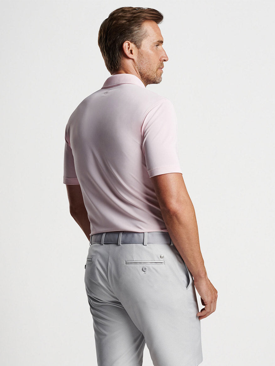 Man wearing a Peter Millar Soul Performance Mesh Polo in Misty Rose and gray trousers viewed from behind, exemplifying golf style.