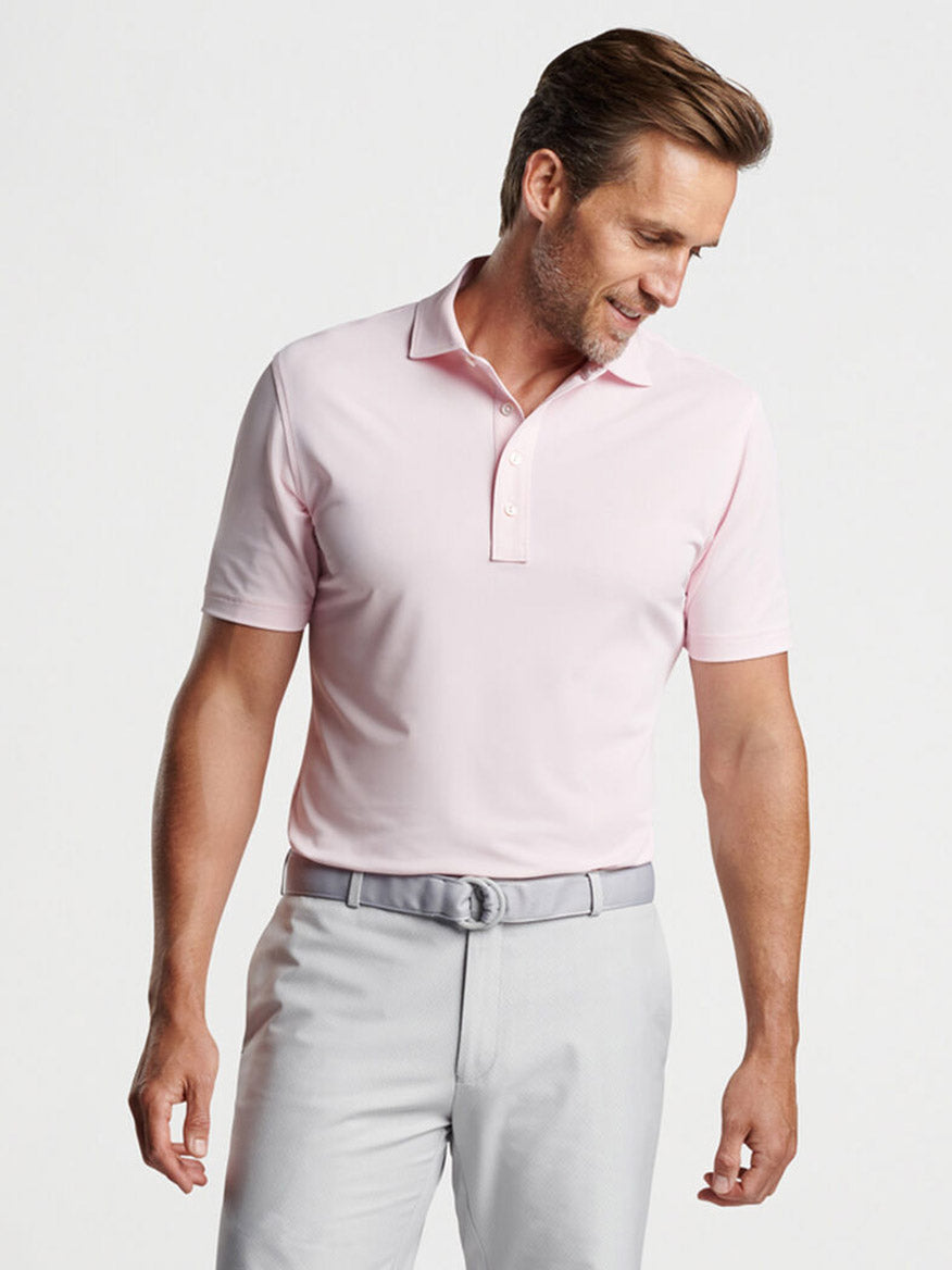 Man wearing a Peter Millar Soul Performance Mesh Polo in Misty Rose and gray trousers looking to the side.