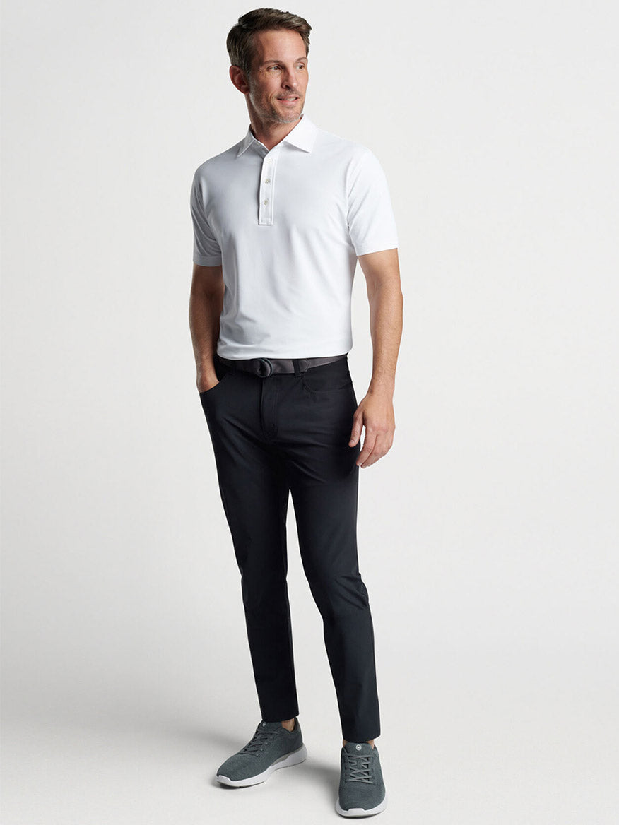 Man posing in a Peter Millar Soul Performance Mesh Polo in White and black trousers with gray sneakers.