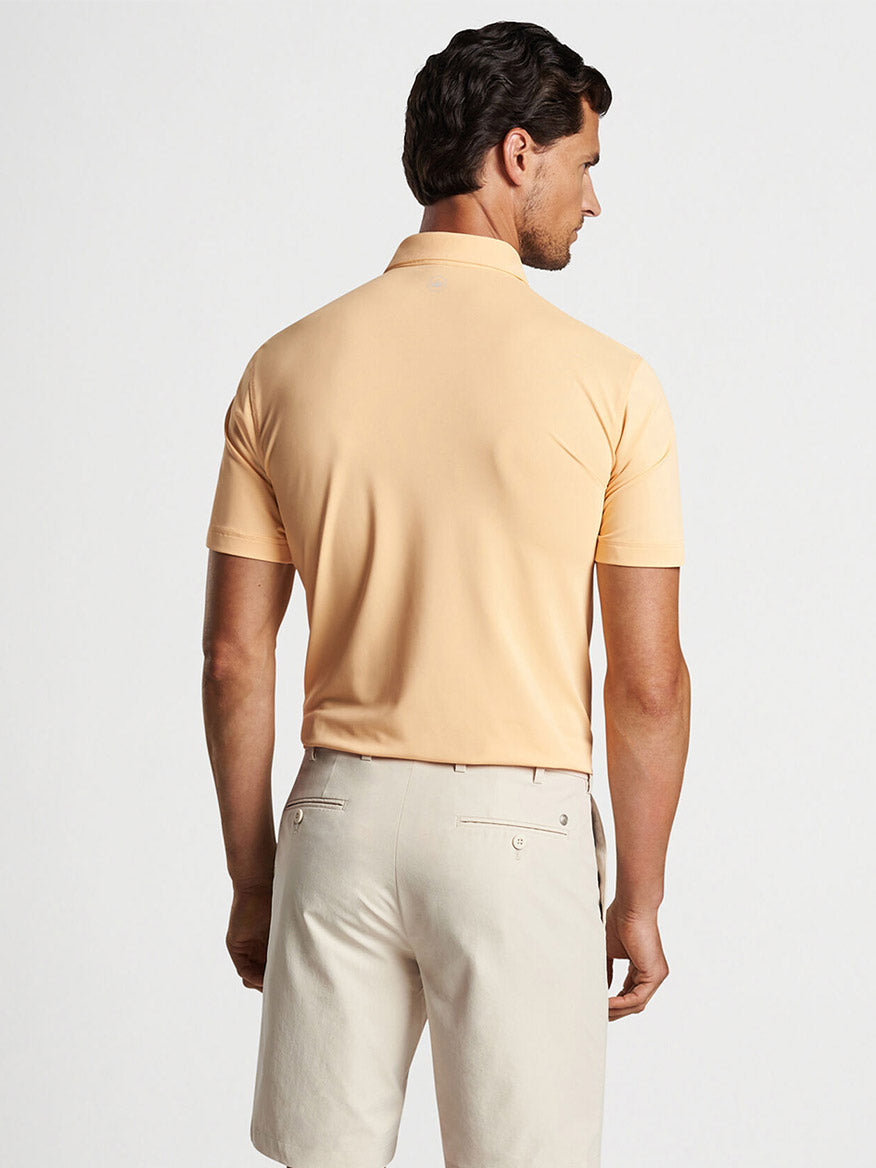 Man viewed from behind wearing a Peter Millar Soul Performance Mesh Polo in Orange Sorbet and light-colored pants.