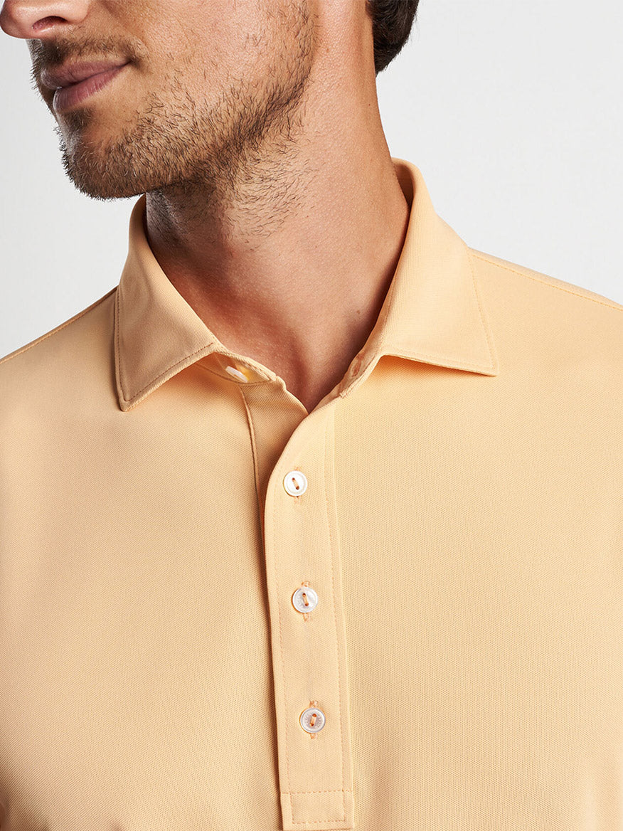 Man in a Peter Millar Soul Performance Mesh Polo in Orange Sorbet with a focus on the collar and buttons.