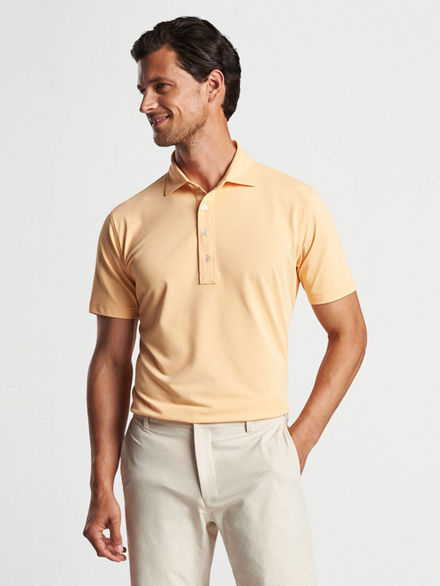 Man wearing a Peter Millar Soul Performance Mesh Polo in Orange Sorbet and cream pants, looking to the side with a smile.