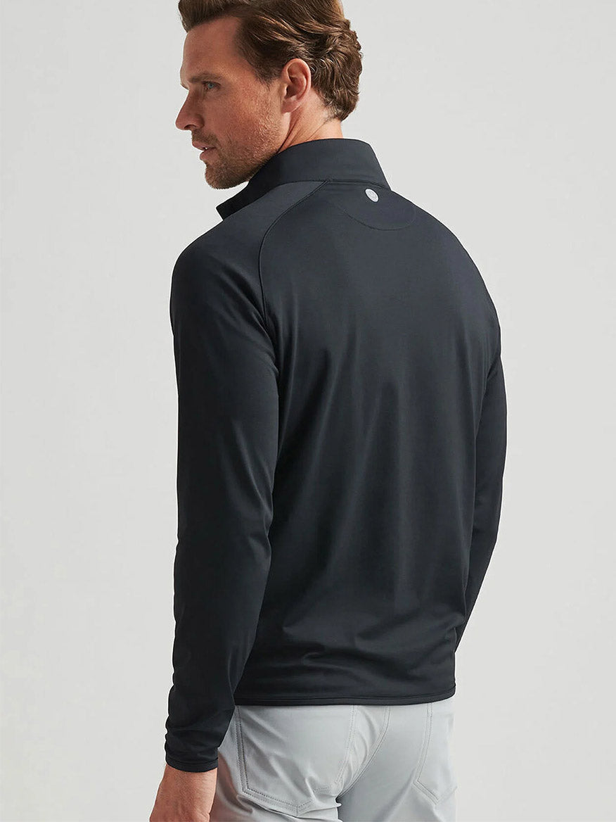 A man with light brown hair, wearing the Peter Millar Stealth Performance Quarter-Zip in Black and light gray pants, stands facing away from the camera.