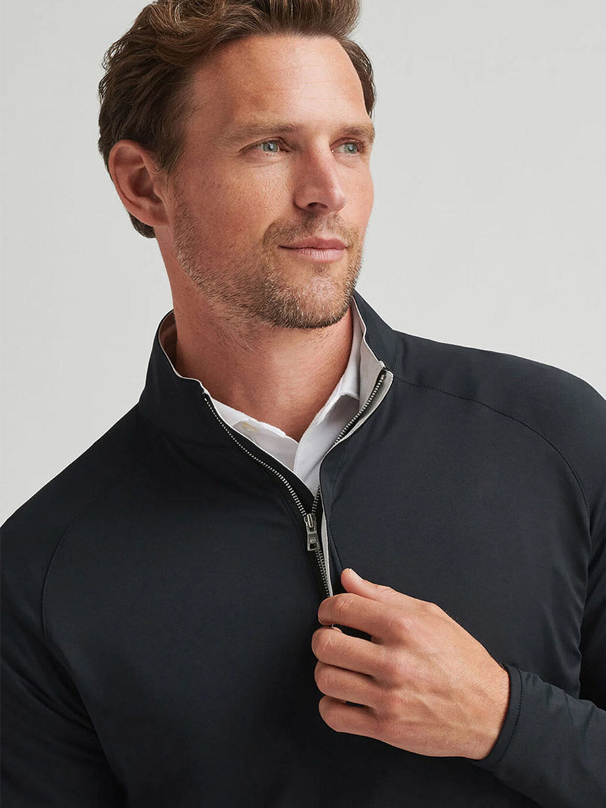 A man with short brown hair and a trimmed beard wears the Peter Millar Stealth Performance Quarter-Zip in Black over a white collared shirt, looking slightly to the side against a neutral background.