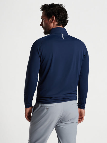 Sentence with product name: Man wearing a Peter Millar Stealth Performance Quarter-Zip in Navy and light gray pants standing with his back to the camera.